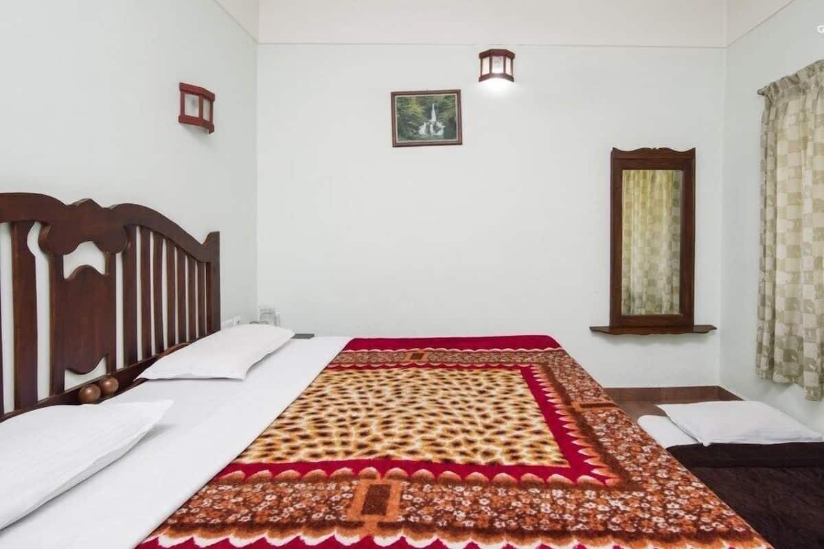 A bedroom with a wooden headboard, a patterned bedspread, a single bed, a nightstand, a wall-mounted lamp, a framed picture, and a window with curtains.