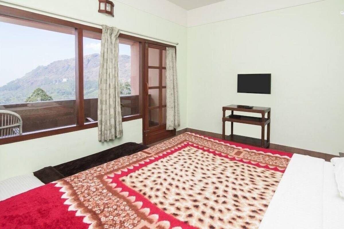 A room with a large window, a bed, a TV, and a small table.