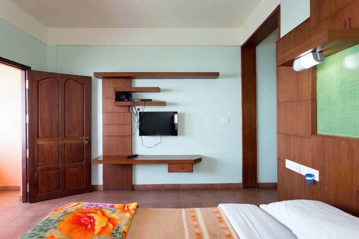 A bedroom with a bed, a TV mounted on the wall, wooden shelves, and a wardrobe.