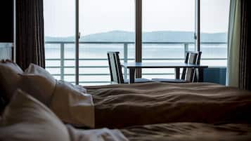 A hotel room with a bed, a small table, and chairs. The room has large windows with a view of the sea and mountains.