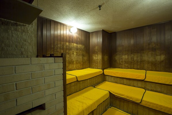 A room with wooden walls and a brick partition. There are multiple beds with yellow bedding.