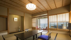 Una habitación japonesa tradicional con suelo de tatami, una mesa baja y puertas correderas que dan a un balcón con vistas.