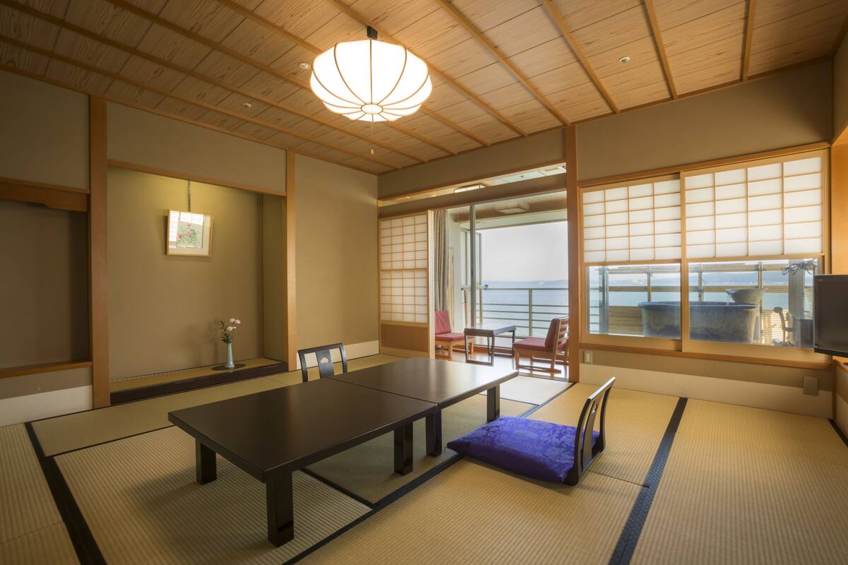 A traditional Japanese room with tatami flooring, a low table, and sliding doors leading to a balcony with a view.