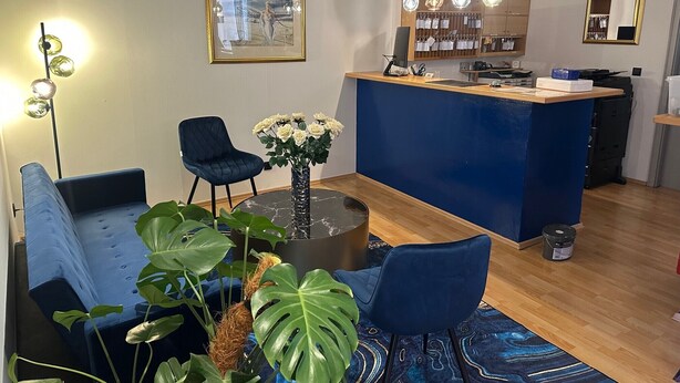 Un intérieur moderne avec un canapé bleu, une table ronde ornée d’un vase de fleurs, une chaise bleue, un comptoir d’accueil et un grand miroir.