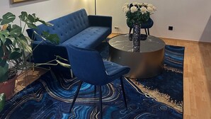 Un salon moderne avec un canapé bleu, une table basse ronde, une plante en pot et un téléviseur à écran plat fixé au mur.