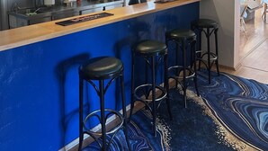Un espace bar avec un comptoir bleu, des tabourets noirs, un menu écrit à la craie et une horloge au mur.