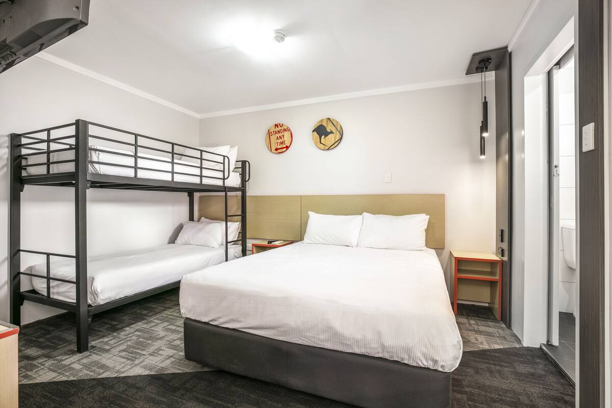 A hotel room with bunk beds, a large bed, bedside tables, and a wall clock.