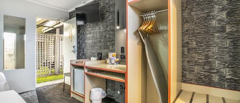Habitación de hotel moderna con kitchenette, un espejo grande, un armario con ropa colgada y vistas al exterior.
