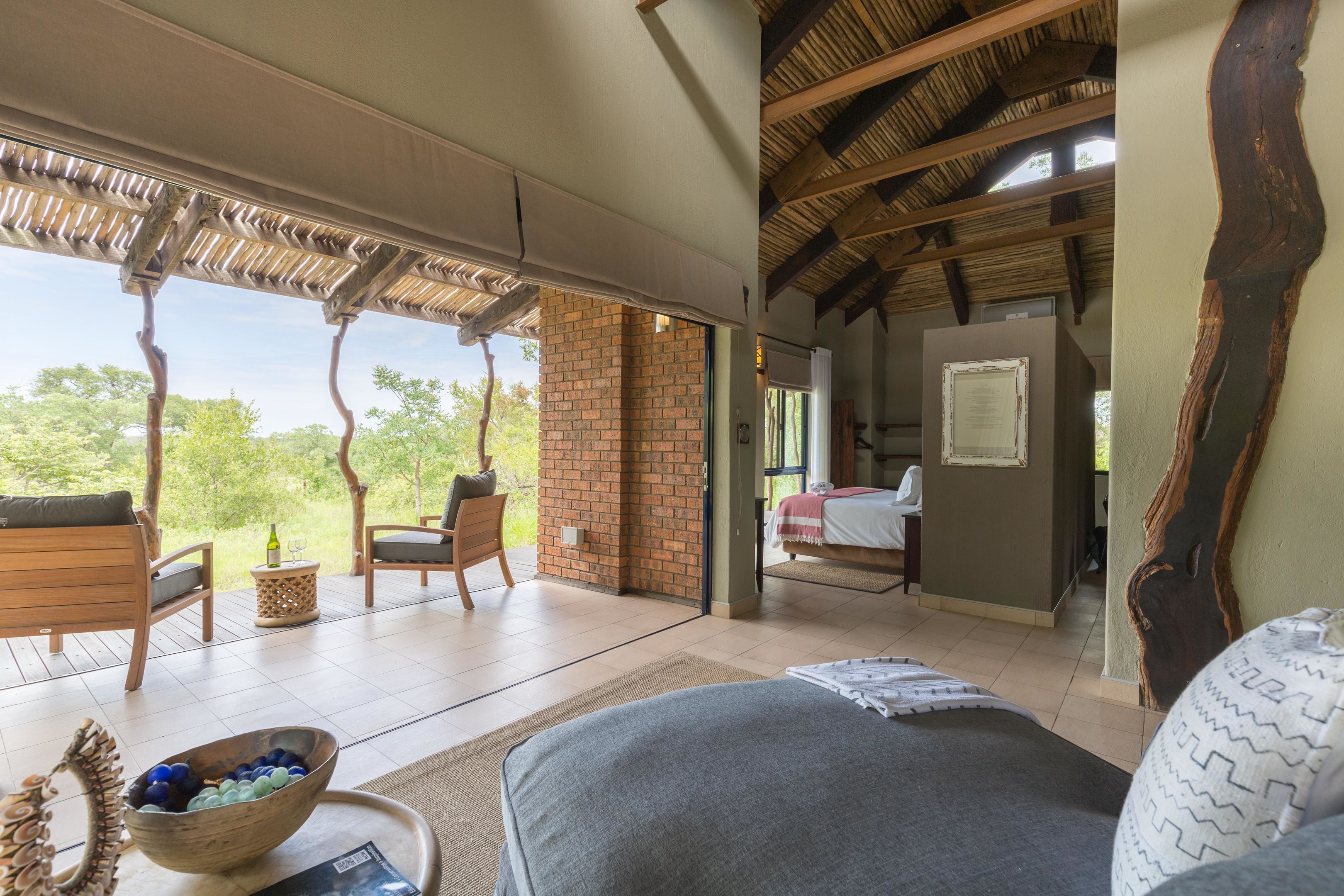A spacious room with a large bed, a wooden chair, a small table with a bowl, and a view of the outdoors.