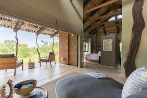 Una habitación amplia con una cama grande, una silla de madera, una mesita con un cuenco y vistas al exterior.