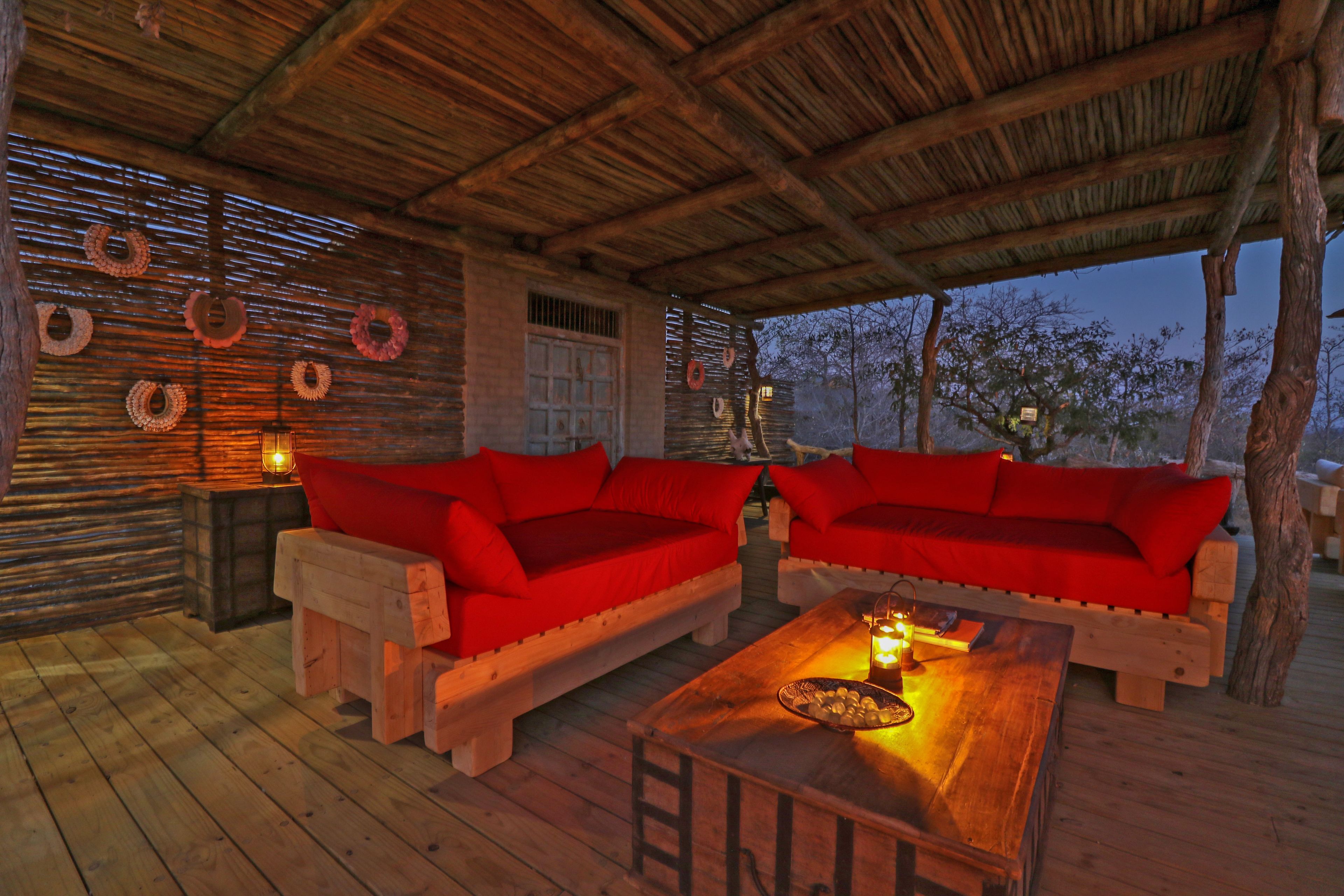 A wooden deck with two red sofas and a wooden table, surrounded by a rustic wooden structure with a thatched roof.