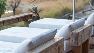 A wooden deck with two white beds, each with a pillow, under a white umbrella.