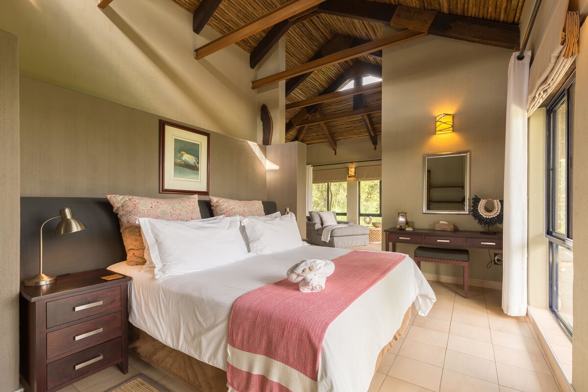 A bedroom with a bed, bedside table, dresser, mirror, and a window with curtains.
