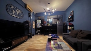 A living room with a large flat-screen TV, a coffee table with a board game, a sofa, and a kitchen area in the background. - Kenting Timehouse (Hengchun)