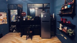 A compact kitchen with a refrigerator, a dining table, and chairs. There is a chalkboard on the wall and a shelf with decorative items. - Kenting Timehouse (Hengchun)