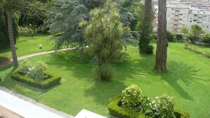 Un jardín bien cuidado con diversos árboles y arbustos, un sendero despejado y una vista de una zona residencial al fondo.