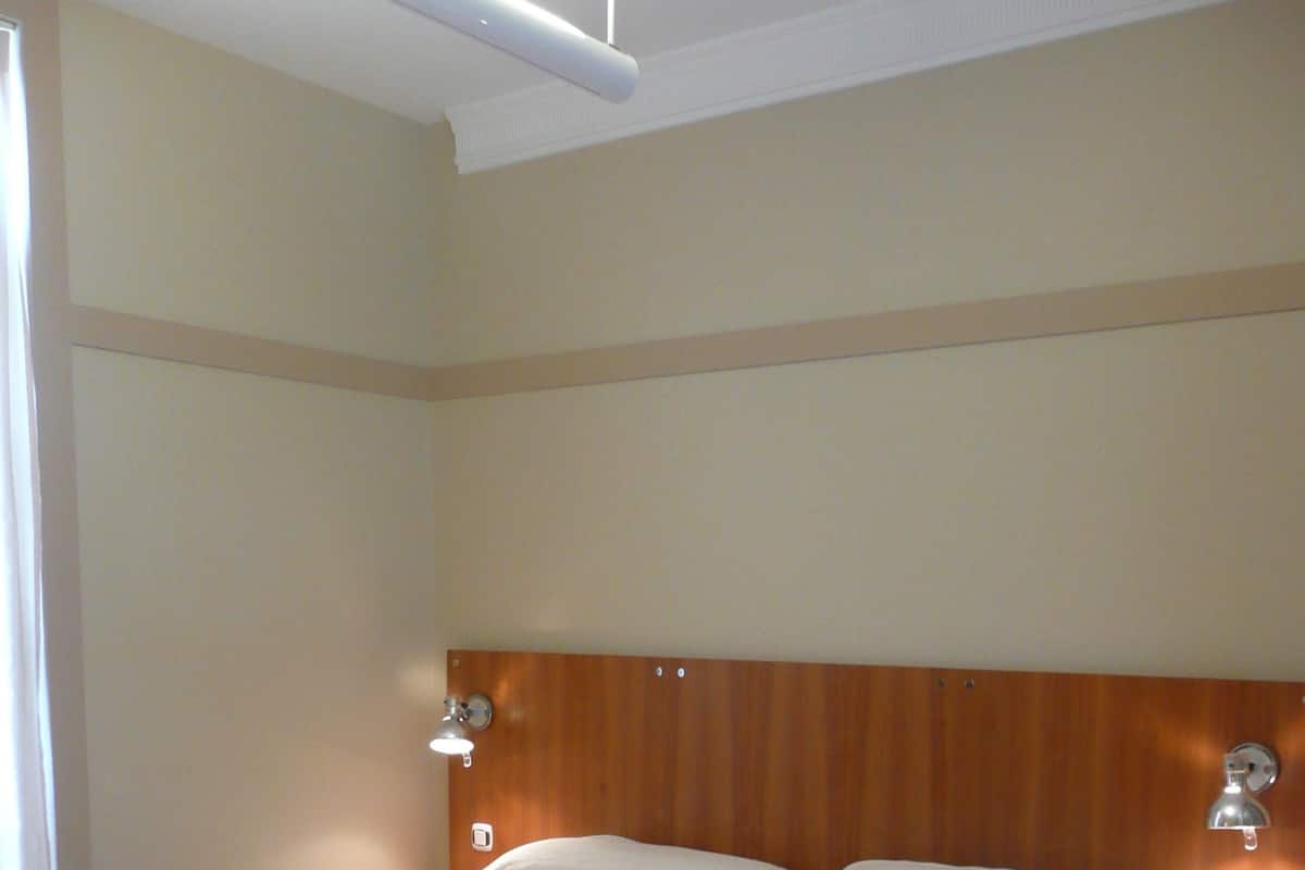 A double bed with white linens in a room with wooden flooring and a wooden headboard.
