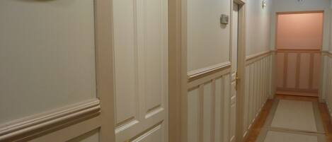 Un pasillo con puertas blancas, una placa con el número 103 sobre una puerta y un interruptor de luz en la pared.