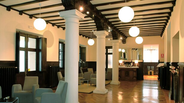Un vestíbulo amplio con suelos de madera, columnas blancas y luminarias modernas.