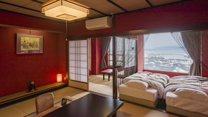 A traditional Japanese-style room with tatami flooring, a low table, a bed with white bedding, and a view of a cityscape through large windows. - Wajimaonsen Yashio (Wajima)
