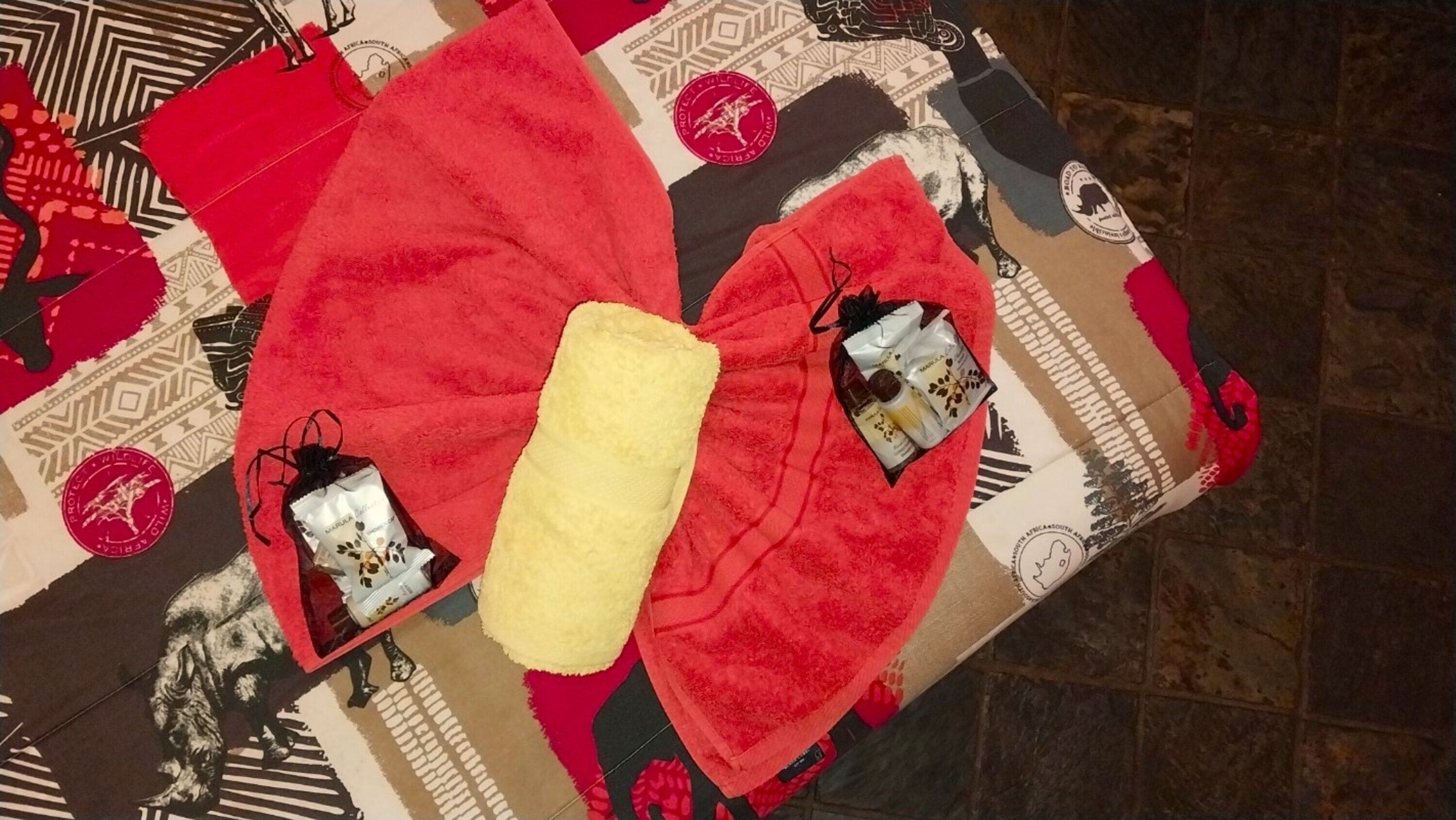 A room with a patterned floor, a red sofa, a yellow cushion, and a small table with a bottle and a bag.