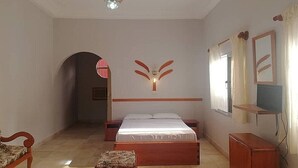 A bedroom with a bed, a wooden nightstand, a dresser, a chair, and a chandelier. - Sermaho Residence - Adults Only (Serrekunda)
