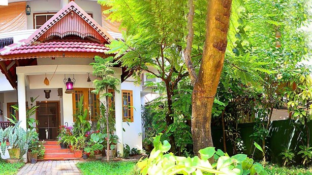 A traditional house with a tiled roof, surrounded by lush greenery and potted plants. - Heavenly Homestay (Kochi)