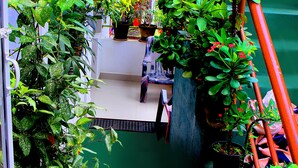 A narrow indoor space with multiple potted plants arranged along the walls and a staircase with red railings. - Heavenly Homestay (Kochi)