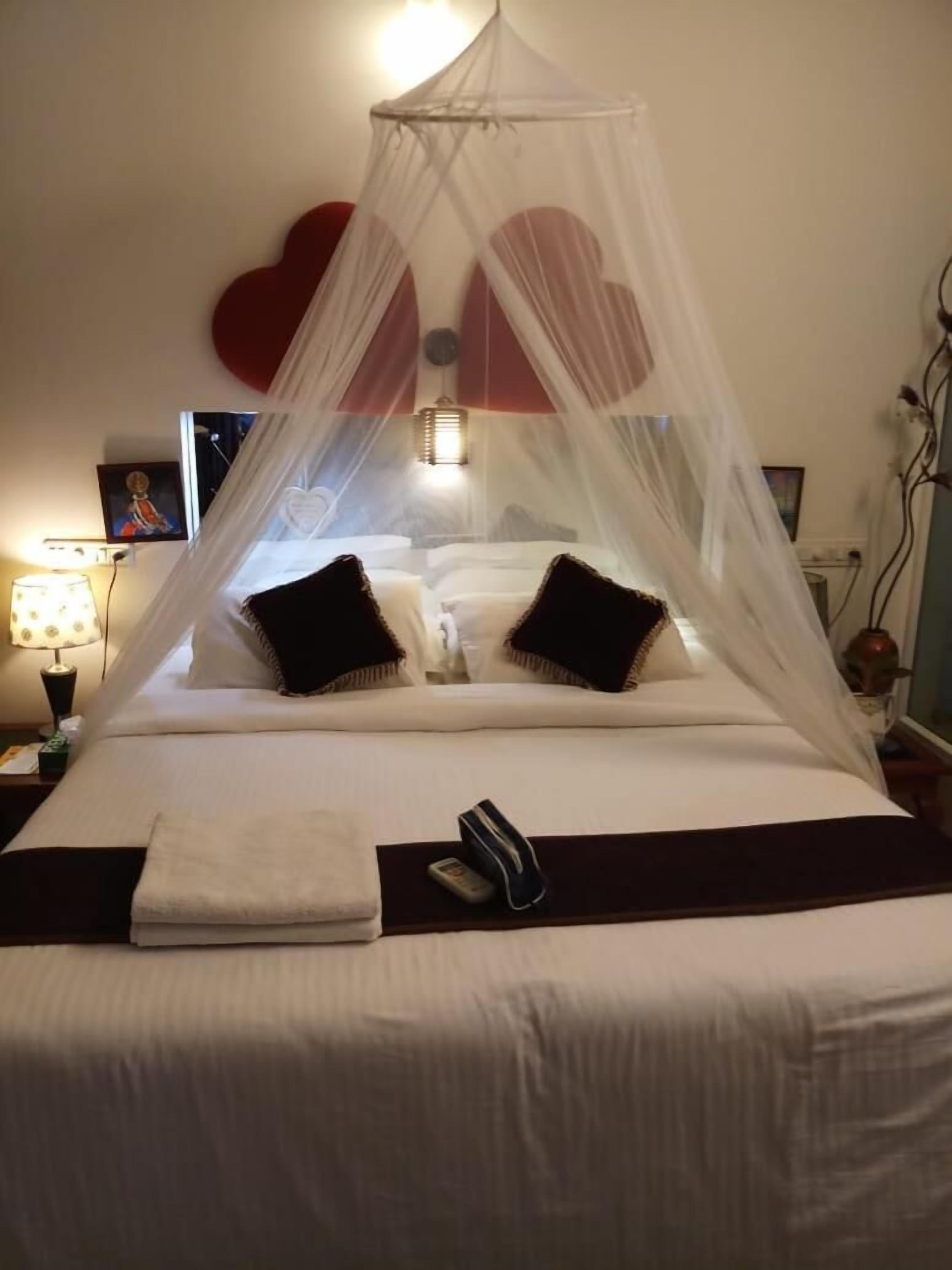 Een bed met hemelbed, kussens, een nachtkastje met lamp en een muur met hartvormige decoraties.