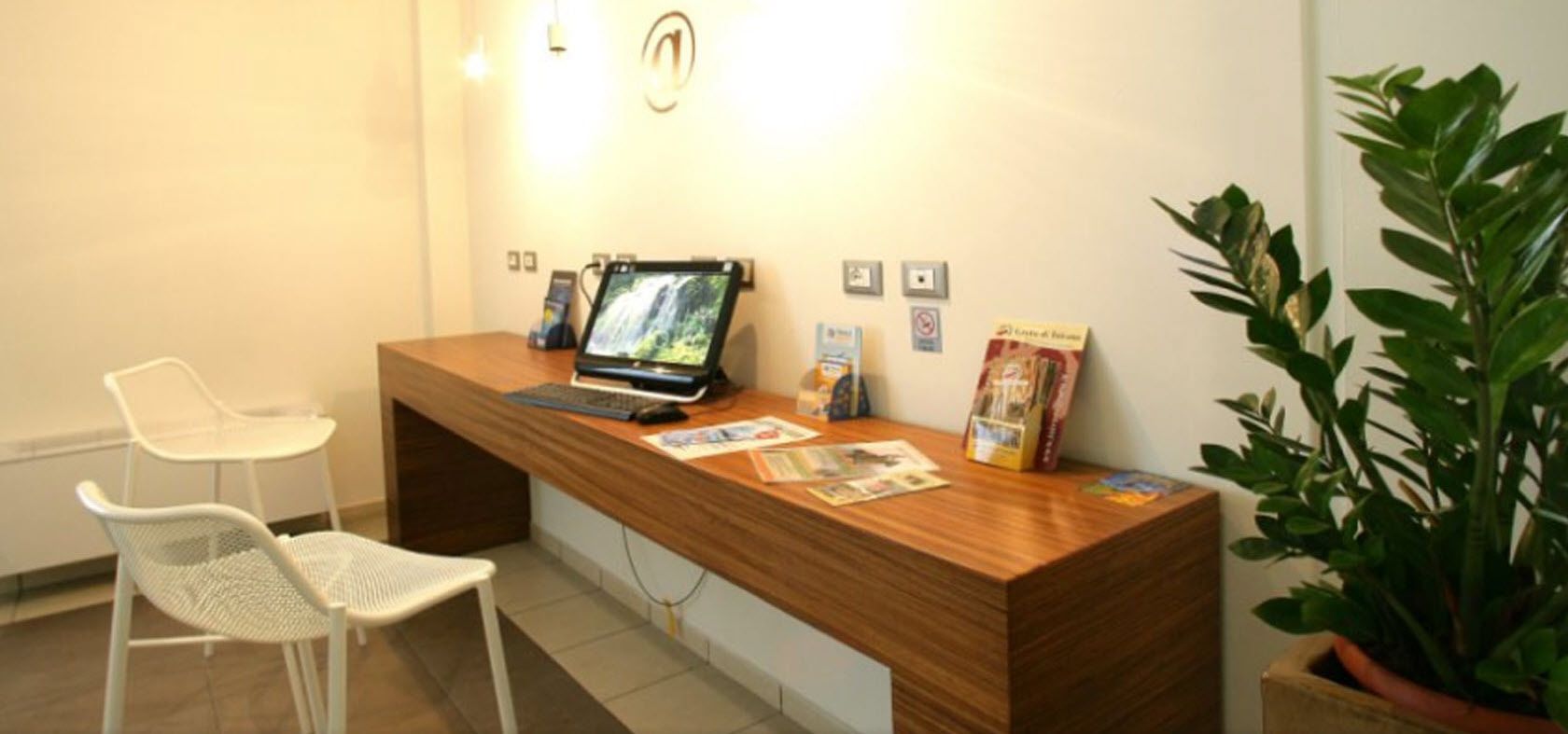 Un comptoir d’accueil avec un ordinateur portable, des brochures et une plante.