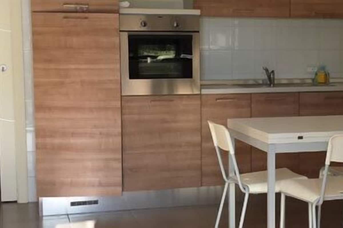 A modern kitchen with wooden cabinets, a built-in oven, and a white dining table with chairs.