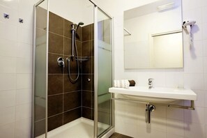Un baño moderno con ducha de vidrio, un lavamanos blanco y un espejo encima.