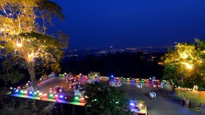 Een avondevenement buiten met tafels en stoelen op een houten terras, omringd door bomen en verlicht met lichtslingers.