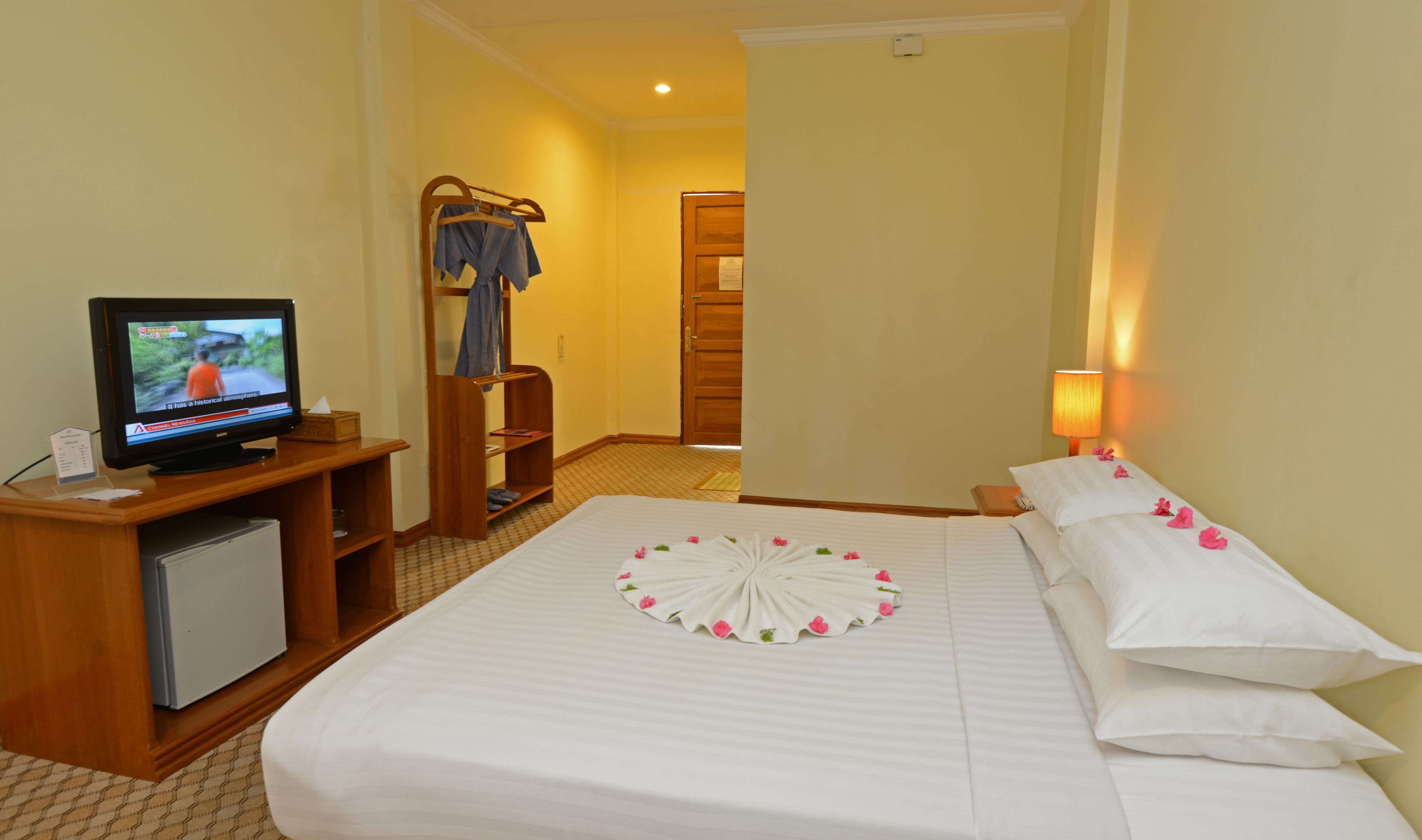 Une chambre d’hôtel comprenant un lit, une télévision, un bureau en bois et une porte donnant sur une autre pièce.