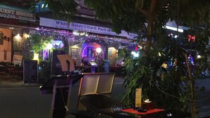 An outdoor seating area with tables and chairs, a sign for 'White River Back Pack House', and a restaurant named 'Guest House' in the background. - Golden World Guesthouse (Phnom Penh)