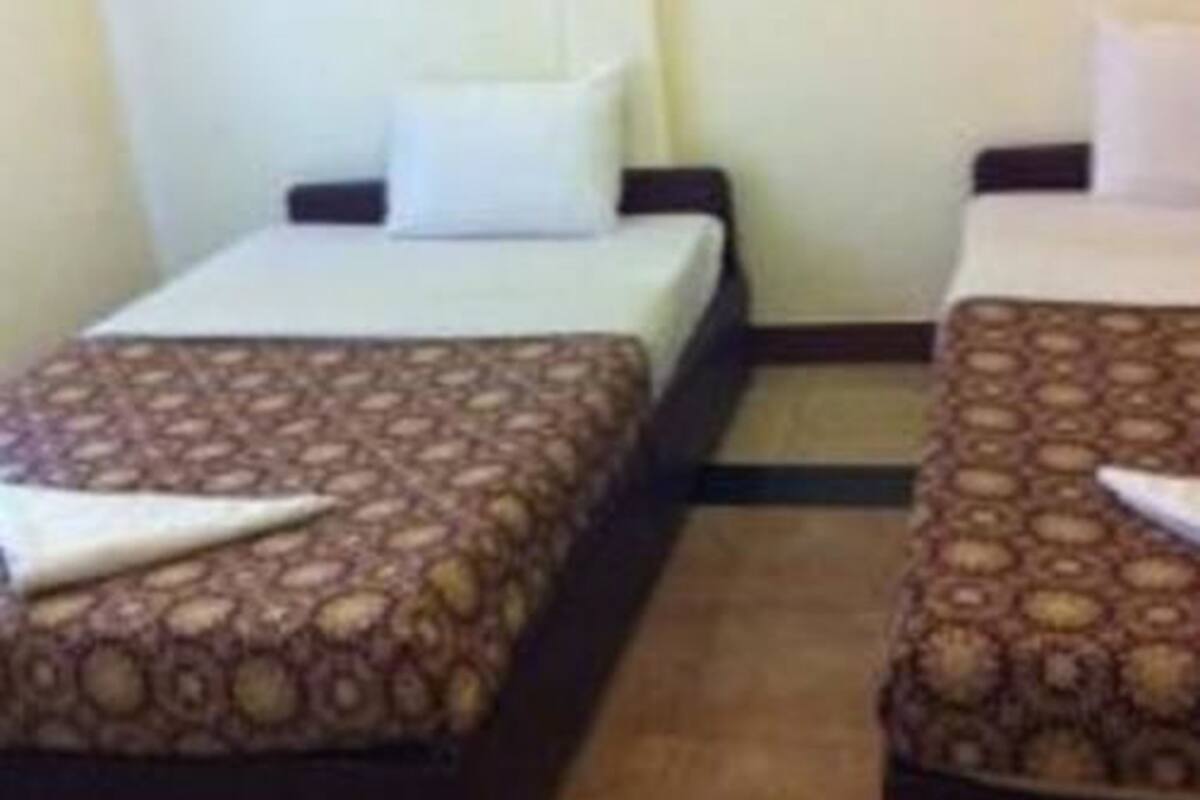A small hotel room with two single beds, each with a patterned bedspread and a pillow.