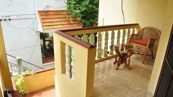 A balcony with a tiled floor, a wicker chair with a cushion, and a small table with a bowl and a book.