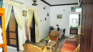 A traditional room with a dining area, wicker furniture, and a red sofa. - Lazar Residency Homestay (Kochi)
