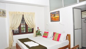 A bedroom with a bed, a window with curtains, a painting, and a refrigerator. - Lazar Residency Homestay (Kochi)