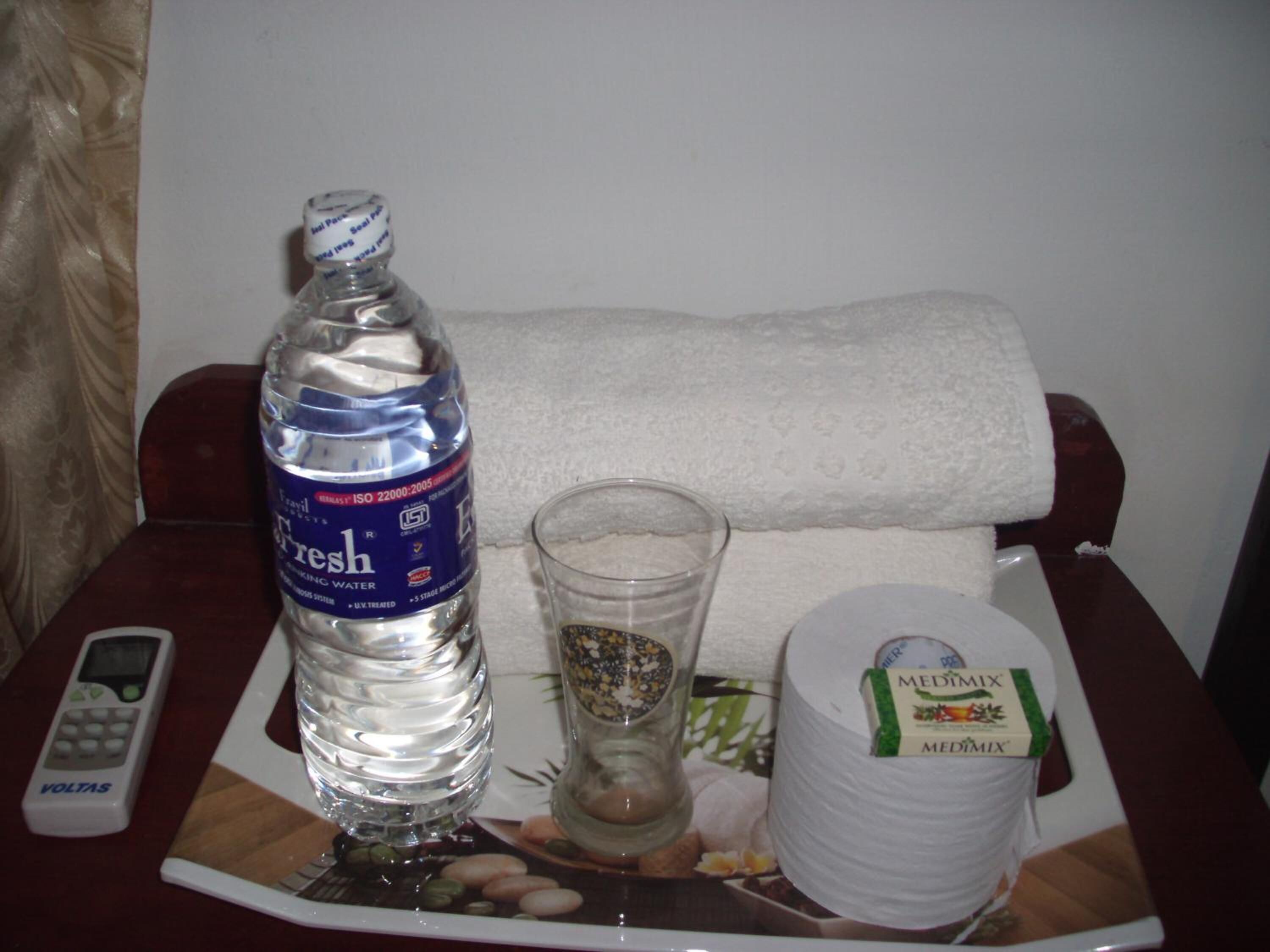Una botella de agua, un vaso, un pañuelo y un control remoto sobre una bandeja.