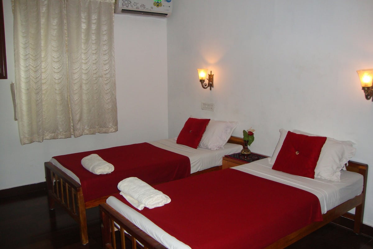 A hotel room with two single beds, each with a red bedspread and white pillows. There are two wall-mounted lamps on either side of the beds.