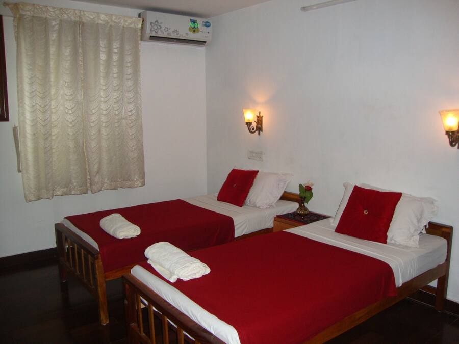 Habitació d'hotel amb dos llits individuals, cadascun amb una mantella vermella i almoines blanques. Hi ha dues làmpades fixades a la paret, una a cada costat dels llits.