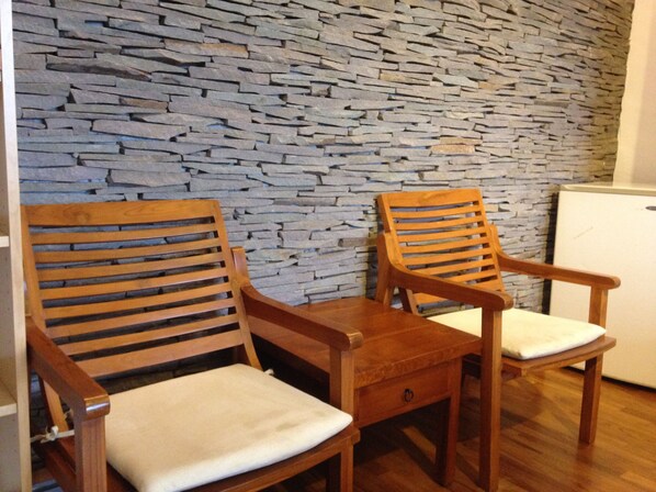 Two wooden chairs with white cushions against a stone wall.