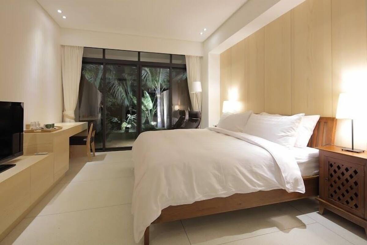 Una habitación de hotel moderna con una cama grande, un televisor, un escritorio y vistas al exterior.