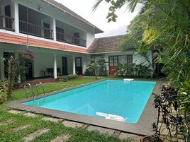 A swimming pool surrounded by a garden with a two-story house in the background.