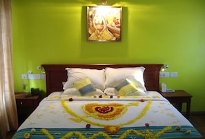 Habitación de hotel con una cama decorada con arreglos florales, una pared verde y un cuadro enmarcado sobre la cama.