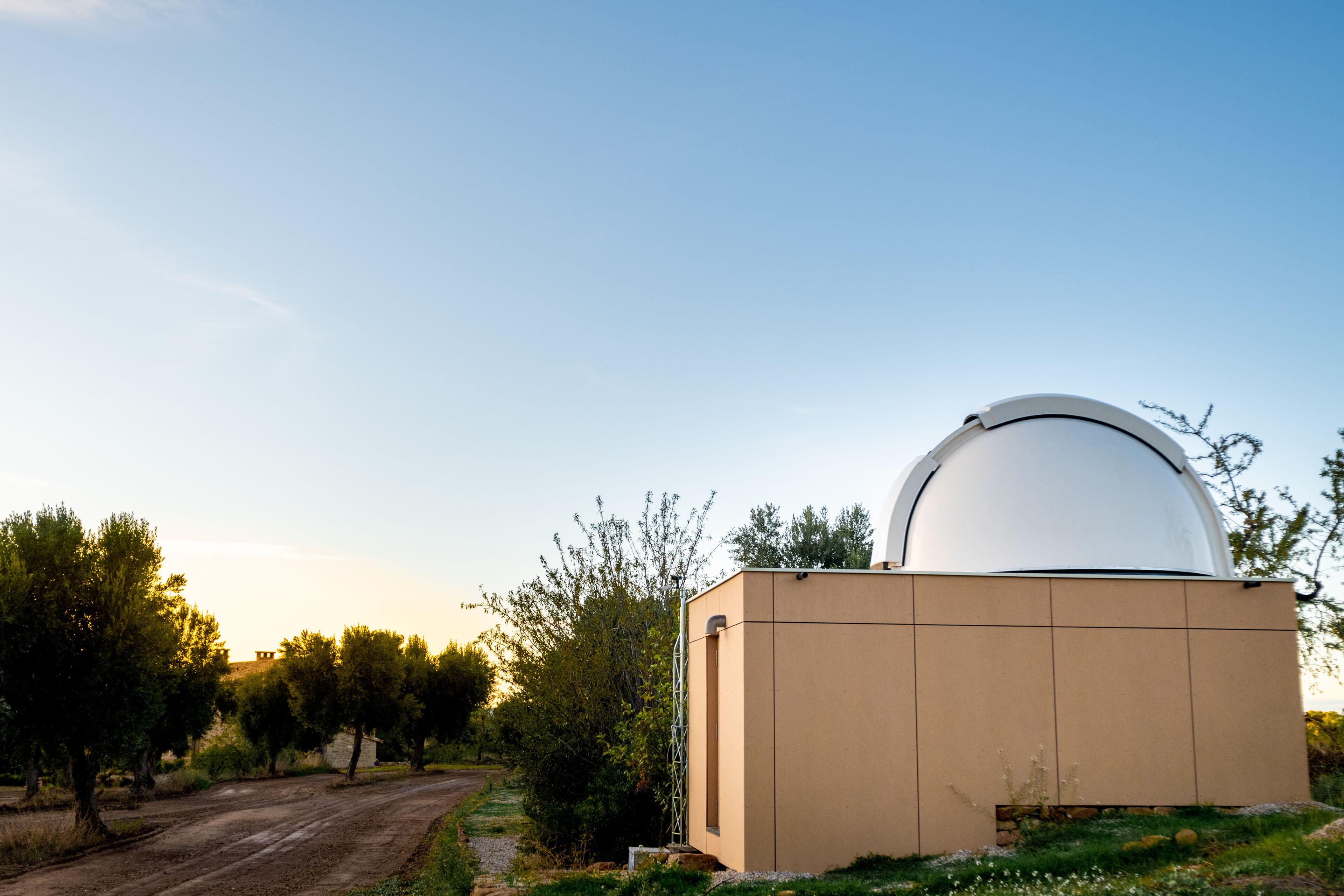 A building with a large dome structure, surrounded by trees and a dirt path.