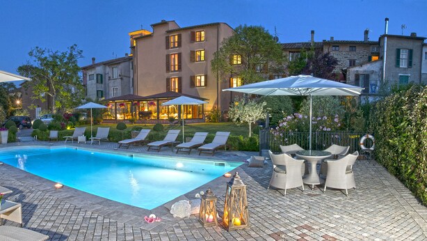 A swimming pool with lounge chairs and umbrellas, surrounded by a brick patio and greenery.