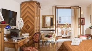 A hotel room with a bed, a desk with a laptop, a chair, a vanity with a mirror, and a balcony with a view.