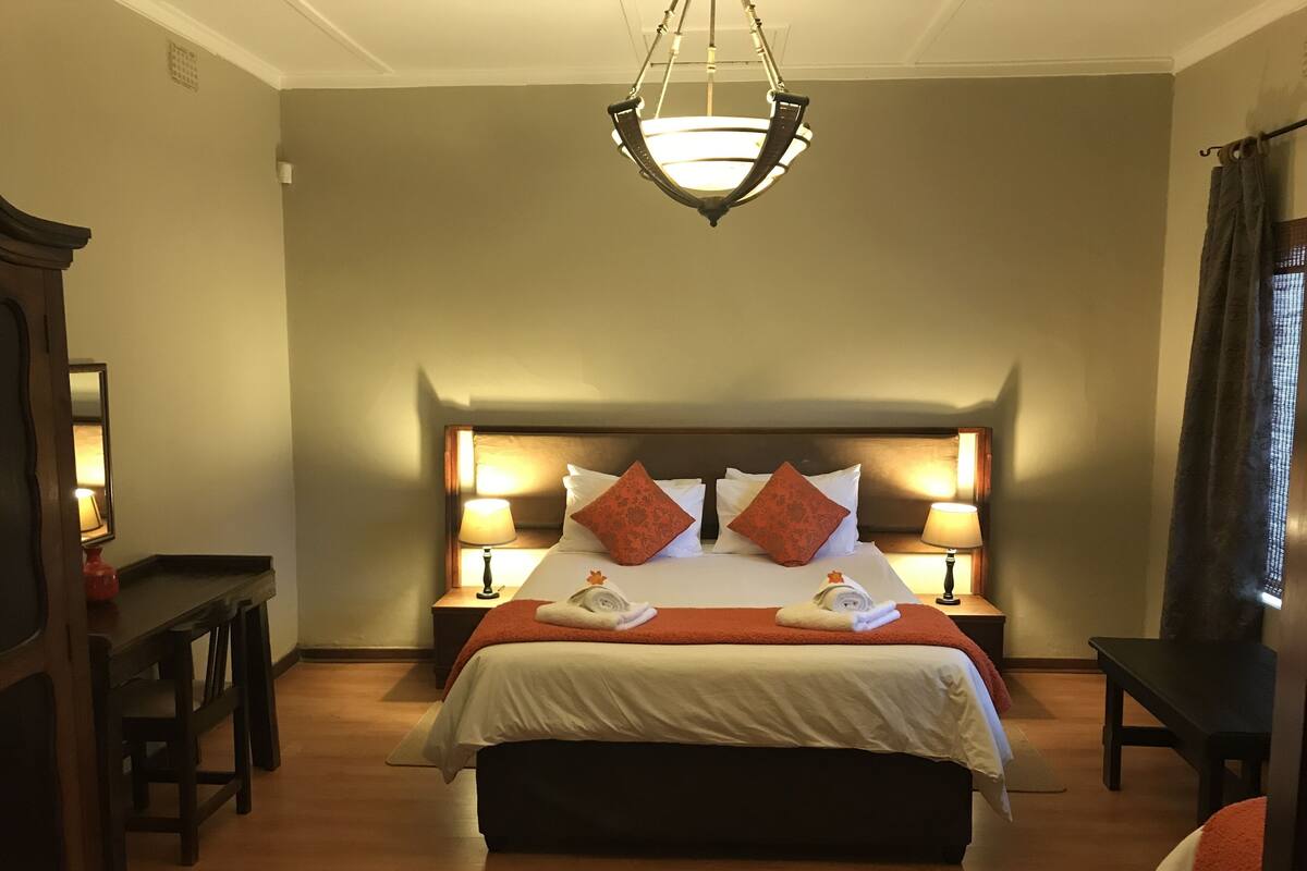 Ein Hotelzimmer mit einem großen Bett, zwei Nachttischlampen, einem hölzernen Kopfteil und einer Deckenleuchte.